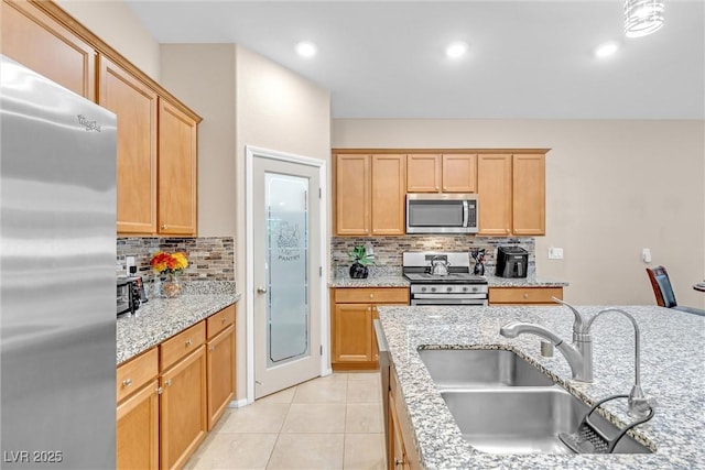 kitchen with appliances with stainless steel finishes, a sink, decorative backsplash, light tile patterned flooring, and light stone counters