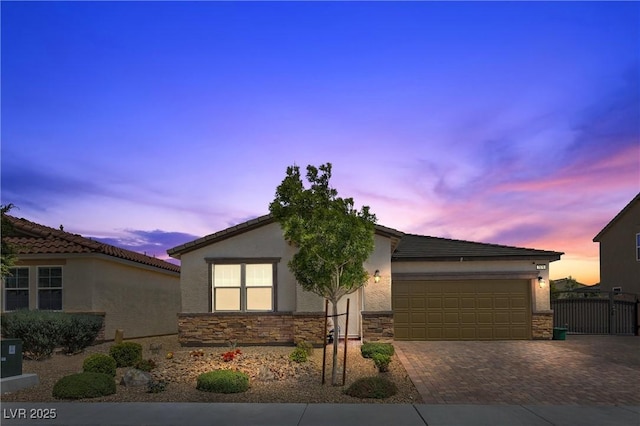 single story home with decorative driveway, a garage, stone siding, stucco siding, and fence