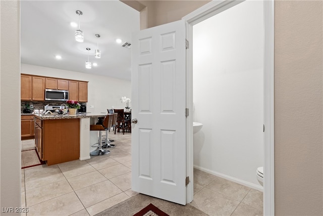 7070 Cinder Horse St, Las Vegas, NV 89131 - kitchen featuring stainless steel microwave, a kitchen breakfast bar, light tile patterned floors, brown cabinets, and decorative light fixtures
