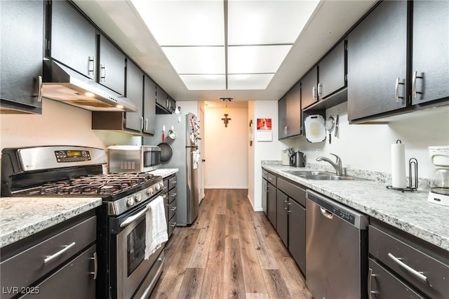 2261 Tall Pine Dr, Las Vegas, NV 89108 - kitchen featuring appliances with stainless steel finishes, a sink, under cabinet range hood, light wood-style floors, and dark cabinetry