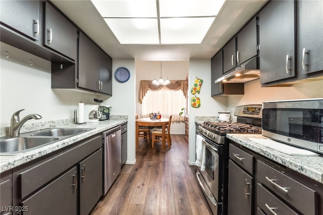 2261 Tall Pine Dr, Las Vegas, NV 89108 - kitchen featuring stainless steel appliances, a sink, under cabinet range hood, a chandelier, and dark wood finished floors