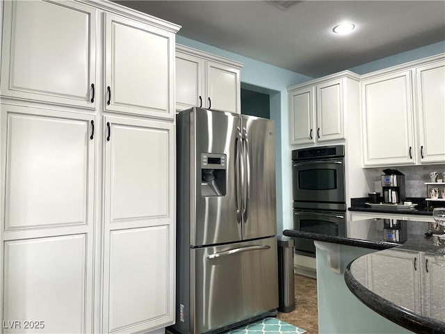 kitchen with stainless steel fridge, multiple ovens, dark stone counters, white cabinets, and recessed lighting