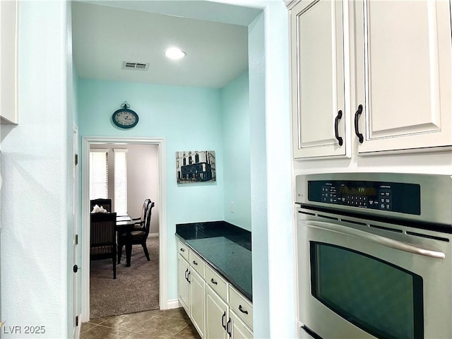 kitchen with stainless steel oven, carpet floors, tile patterned flooring, white cabinetry, and dark stone countertops