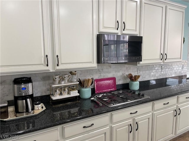 kitchen featuring appliances with stainless steel finishes, white cabinets, decorative backsplash, and dark stone counters