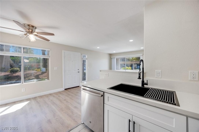 kitchen with dishwasher, a sink, light countertops, light wood finished floors, and white cabinetry