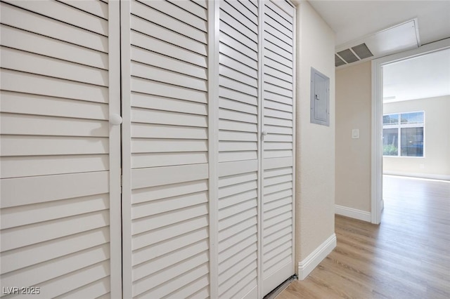 hallway with light wood finished floors, electric panel, and baseboards