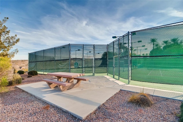 view of home's community featuring a tennis court, fence, and a gate