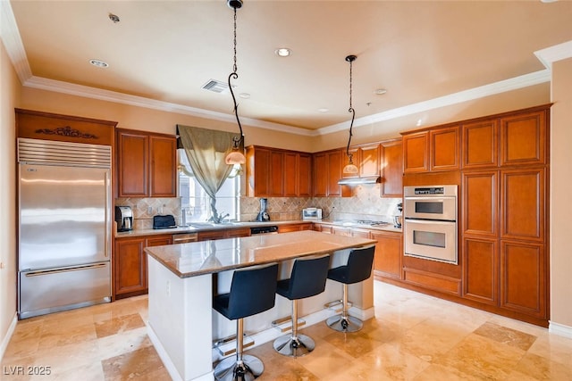 kitchen with appliances with stainless steel finishes, a kitchen island, brown cabinetry, backsplash, and crown molding