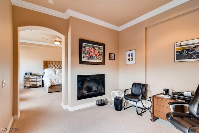 sitting room featuring carpet floors, crown molding, arched walkways, a glass covered fireplace, and baseboards