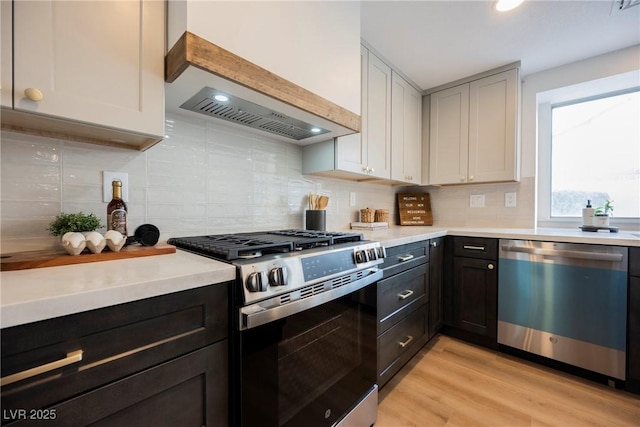 kitchen with stainless steel appliances, custom range hood, light countertops, and backsplash