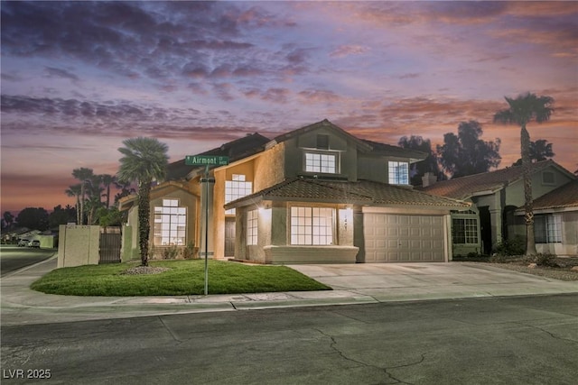 view of front of property with stucco siding, driveway, a tiled roof, an attached garage, and fence