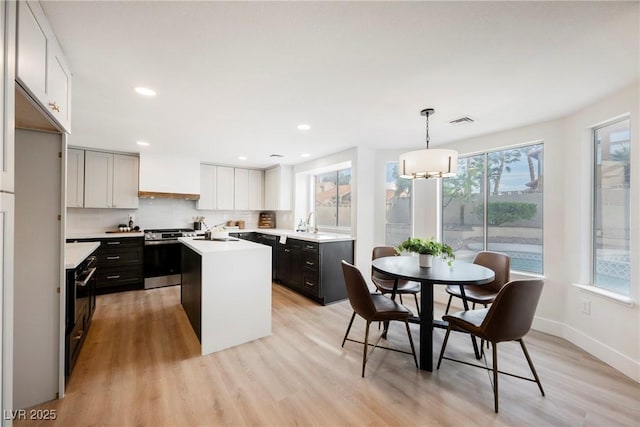 kitchen with stainless steel stove, an island with sink, light countertops, light wood-style floors, and a sink