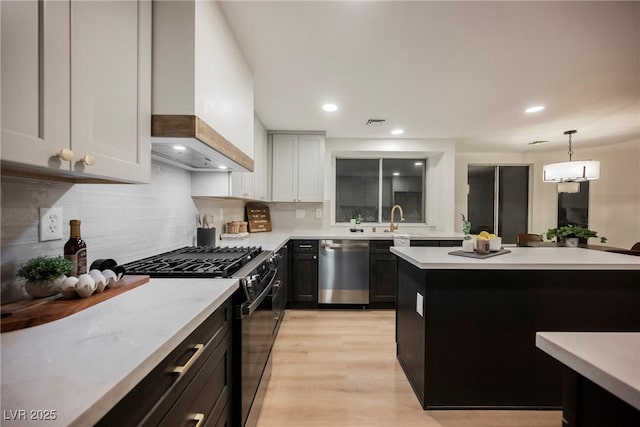 kitchen with dishwasher, range with gas stovetop, light countertops, backsplash, and premium range hood