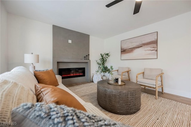 living area with wood finished floors, a glass covered fireplace, a ceiling fan, and baseboards
