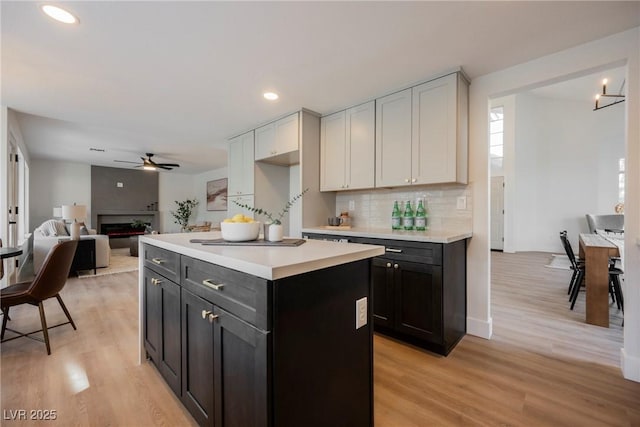 kitchen with a ceiling fan, light wood-style floors, light countertops, tasteful backsplash, and a kitchen island