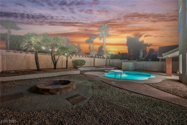 pool at dusk with a fenced backyard, an outdoor fire pit, and a patio area
