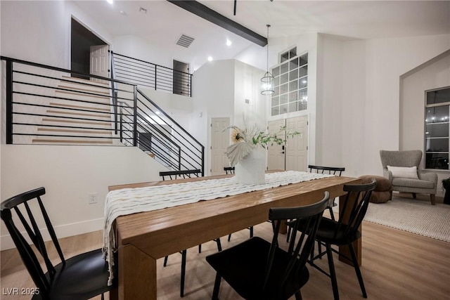 dining space featuring wood finished floors, stairs, beam ceiling, baseboards, and high vaulted ceiling