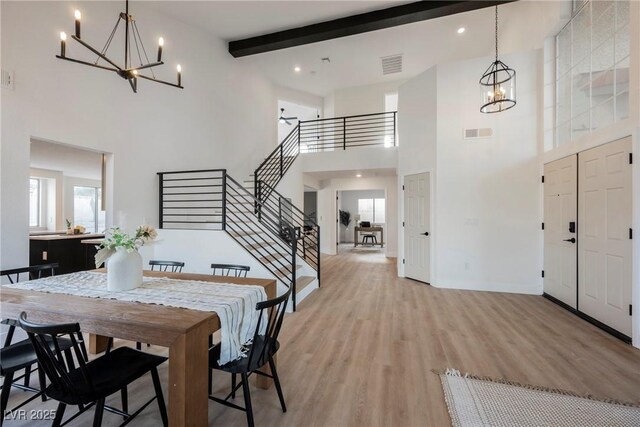 dining space with a chandelier, a high ceiling, stairway, beamed ceiling, and light wood-style flooring