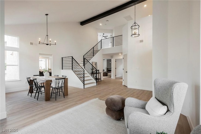 living area with a chandelier, stairway, light wood-style floors, high vaulted ceiling, and baseboards