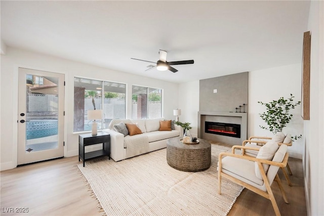 living area with light wood finished floors, a glass covered fireplace, and ceiling fan