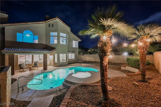 back of house at twilight featuring a fenced backyard, a patio area, a pool with connected hot tub, and stucco siding