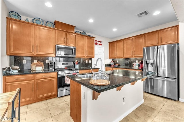 10353 Settlers Run Ave, Las Vegas, NV 89166 - kitchen featuring stainless steel appliances, a sink, an island with sink, brown cabinets, and tasteful backsplash