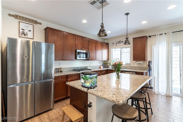 kitchen featuring appliances with stainless steel finishes, light wood-style flooring, a breakfast bar area, a center island, and light stone counters