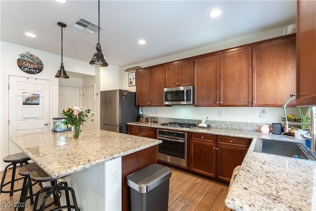 kitchen featuring appliances with stainless steel finishes, a kitchen breakfast bar, light wood finished floors, a sink, and a kitchen island