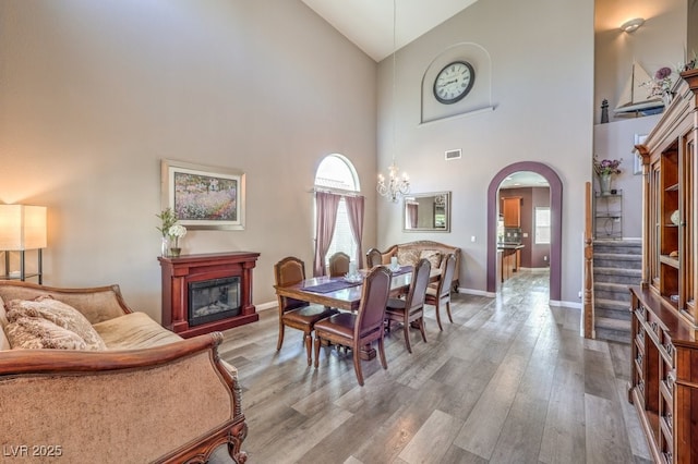 dining room featuring high vaulted ceiling, arched walkways, wood finished floors, baseboards, and a glass covered fireplace