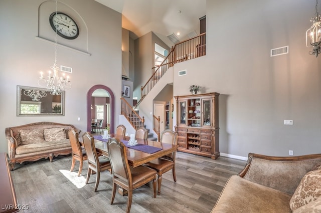 dining area with a chandelier, stairway, arched walkways, wood finished floors, and a towering ceiling