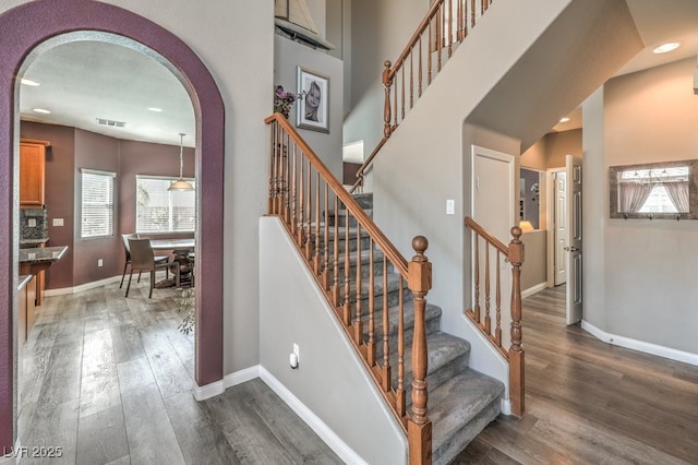 stairway with plenty of natural light, arched walkways, wood finished floors, recessed lighting, and baseboards