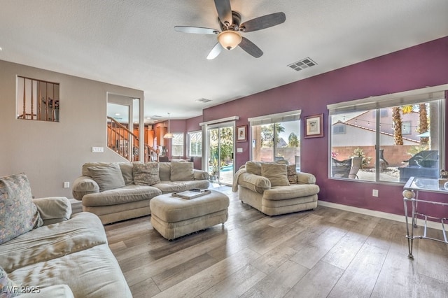 living room featuring stairway, a ceiling fan, wood finished floors, baseboards, and a textured ceiling
