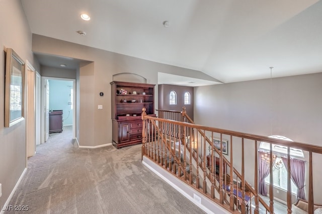 hallway with an upstairs landing, light colored carpet, vaulted ceiling, baseboards, and recessed lighting