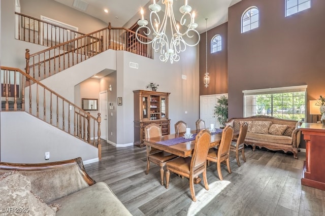 dining room with a towering ceiling, wood finished floors, stairs, a chandelier, and baseboards