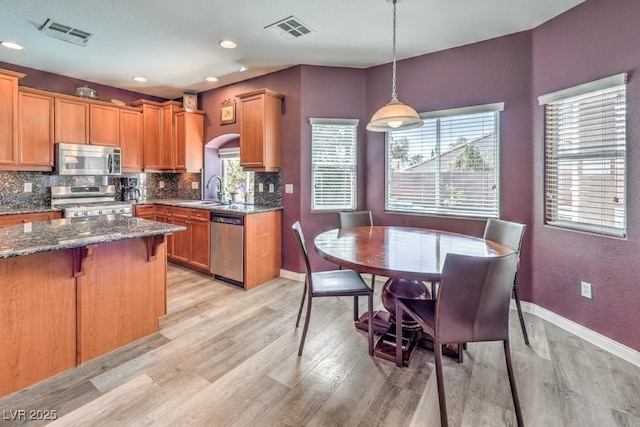 kitchen with stainless steel appliances, tasteful backsplash, light wood-style flooring, dark stone counters, and baseboards