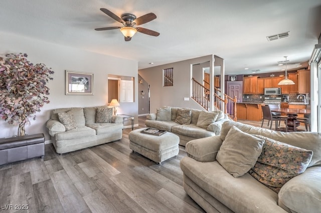 living room featuring stairs, ceiling fan, light wood-style floors, and baseboards