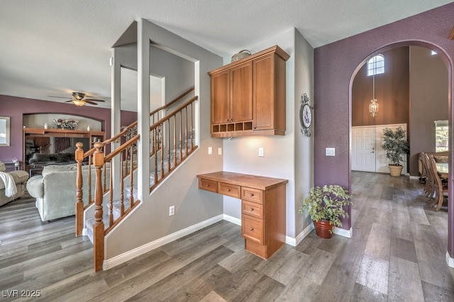 stairway featuring ceiling fan, arched walkways, wood finished floors, and baseboards