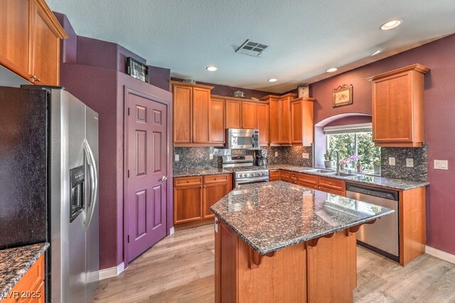 kitchen with appliances with stainless steel finishes, a sink, light wood-type flooring, backsplash, and arched walkways