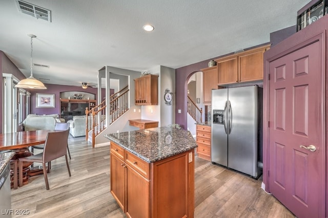 kitchen featuring stainless steel refrigerator with ice dispenser, arched walkways, ceiling fan, a center island, and dark stone counters