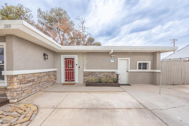view of exterior entry featuring stone siding, stucco siding, fence, and a patio area