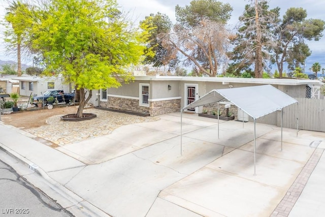 view of front of house with stone siding, concrete driveway, stucco siding, fence, and a detached carport