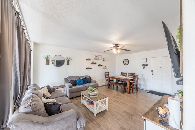 living room with ceiling fan, light wood-type flooring, and a textured ceiling