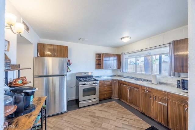 kitchen with appliances with stainless steel finishes, a sink, light countertops, and brown cabinets