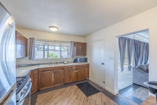 kitchen with appliances with stainless steel finishes, a sink, light countertops, light wood finished floors, and a textured ceiling