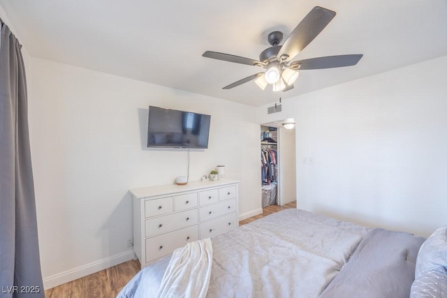 bedroom with light wood finished floors, baseboards, a ceiling fan, and a walk in closet