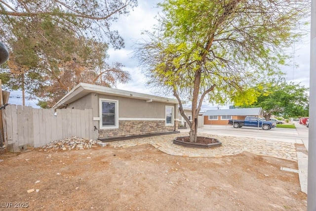 view of front of property with stone siding, fence, and stucco siding