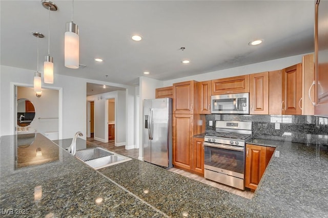 kitchen with appliances with stainless steel finishes, a sink, hanging light fixtures, brown cabinetry, and recessed lighting
