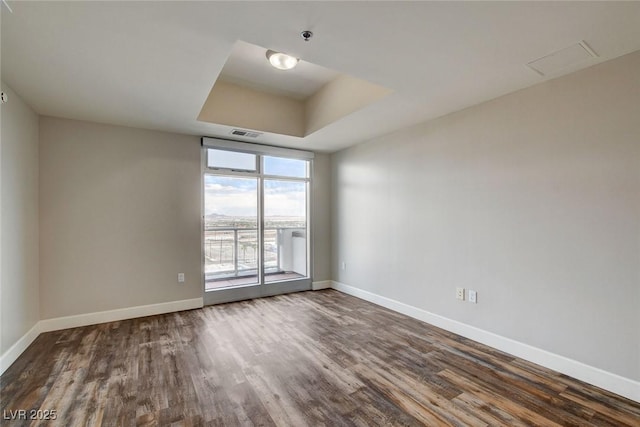 unfurnished room featuring baseboards, wood finished floors, and a raised ceiling