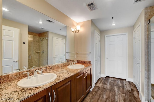 bathroom with a stall shower, wood finished floors, baseboards, double vanity, and recessed lighting