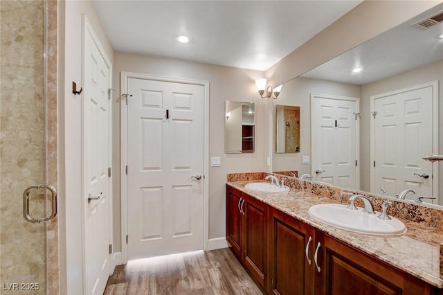 bathroom featuring wood finished floors, baseboards, double vanity, a stall shower, and recessed lighting